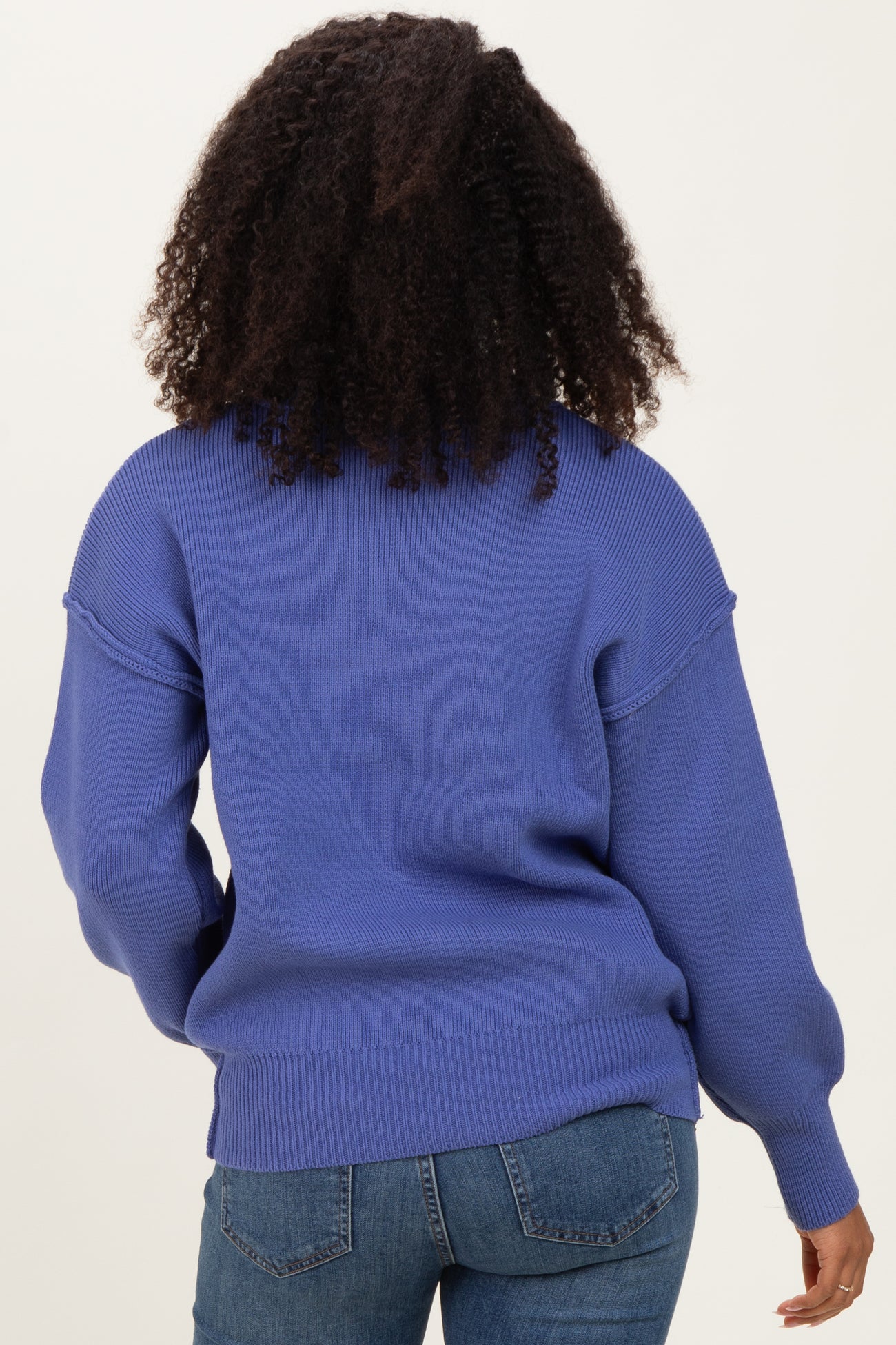 woman wearing a blue oversized sweater with ribbed detailing, viewed from the back, paired with denim jeans