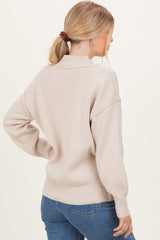 woman wearing a light beige oversized sweater with a high neck and balloon sleeves, styled with blue jeans