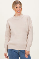 woman wearing a beige ribbed sweater with a high neckline and relaxed fit, paired with blue jeans