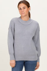 woman wearing a light gray ribbed knit sweater with a high neckline and relaxed fit, paired with blue jeans