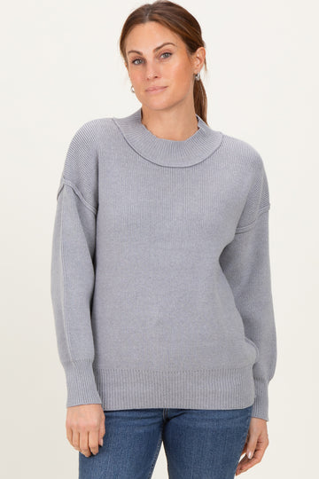 woman wearing a light gray ribbed knit sweater with a high neckline and relaxed fit, paired with blue jeans