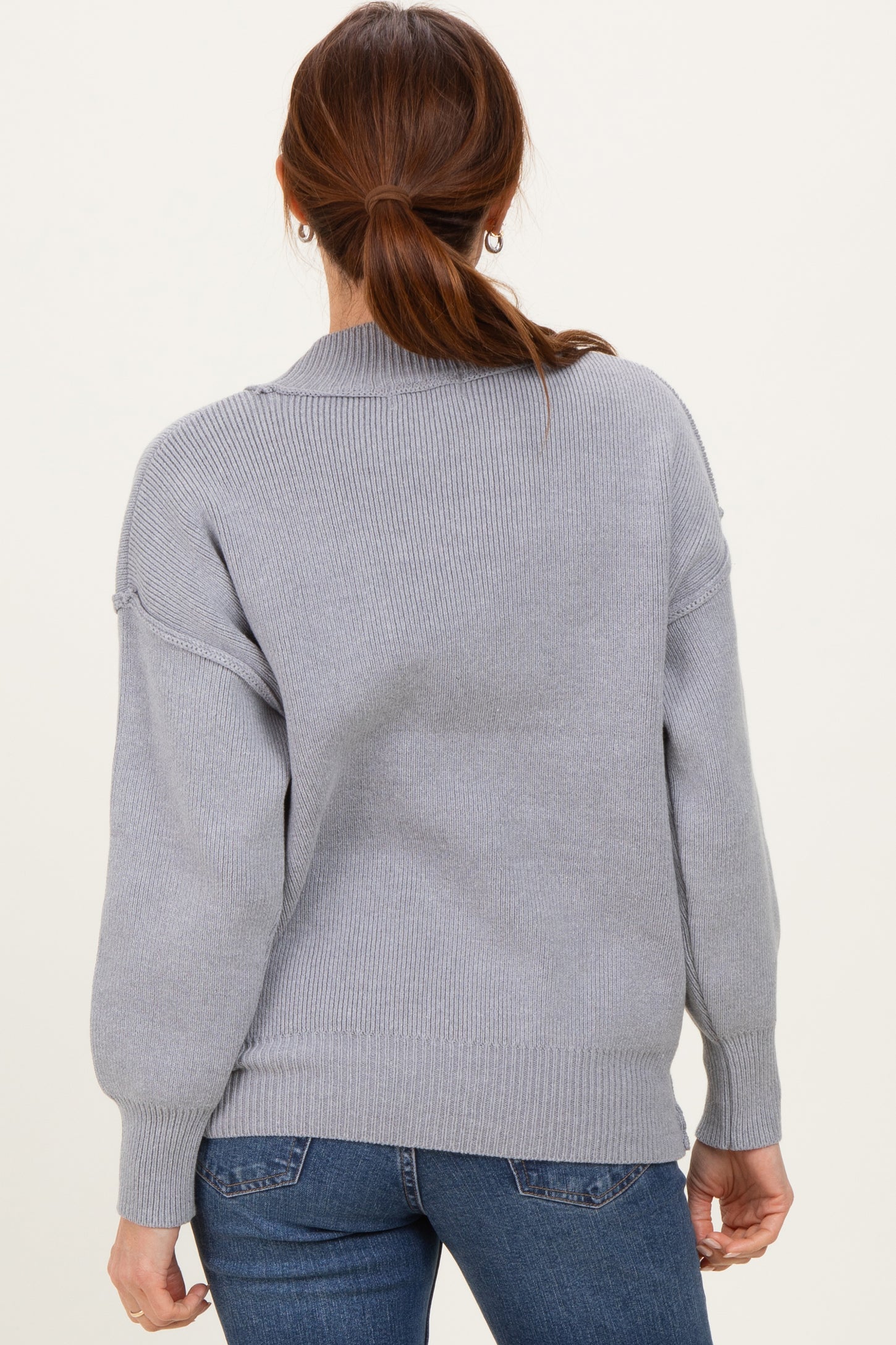 woman wearing a cozy light gray loose-fit sweater with a ribbed texture, seen from the back