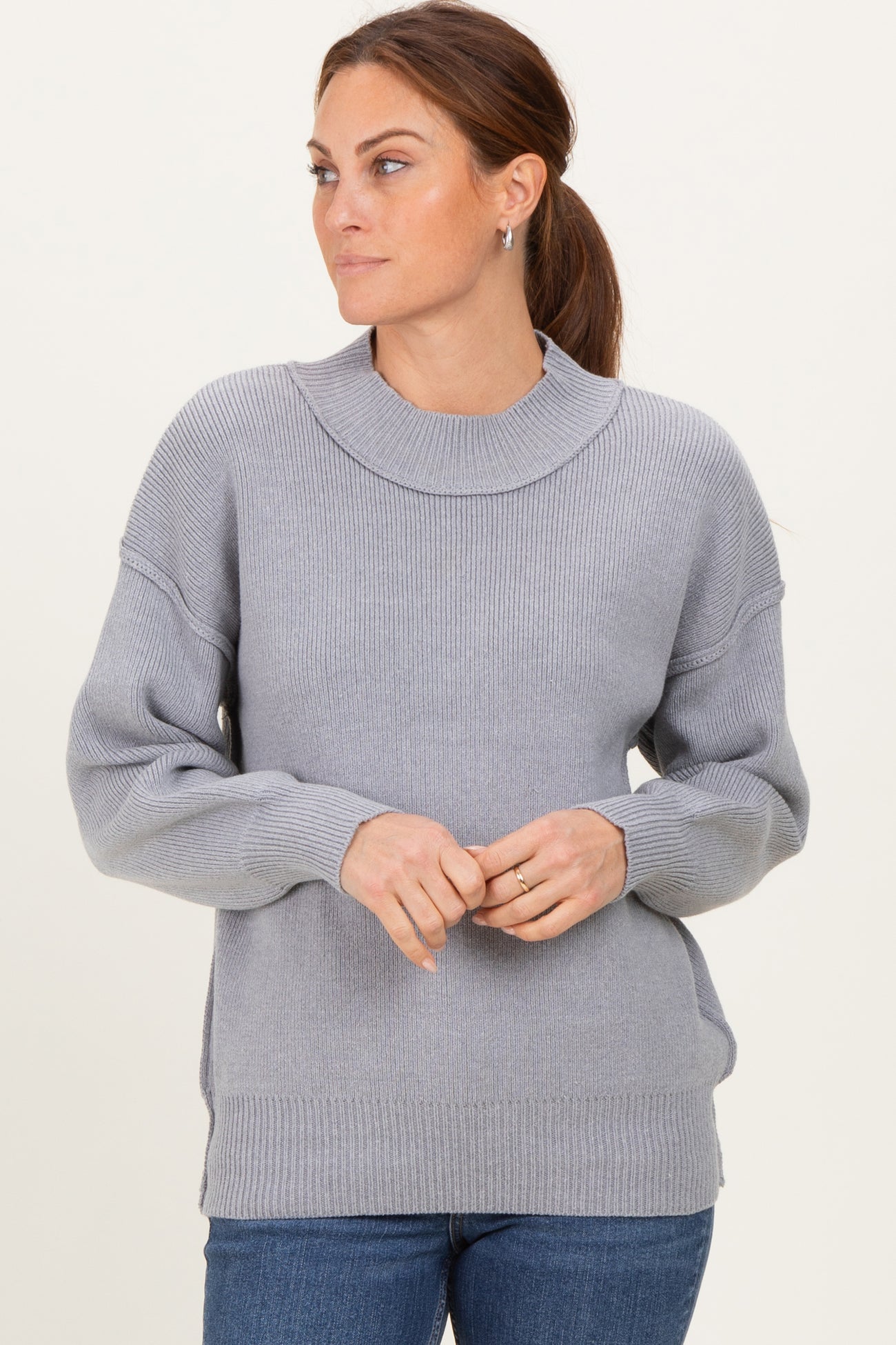 woman wearing a light gray oversized sweater with ribbed texture and a boat neckline, styled with blue jeans