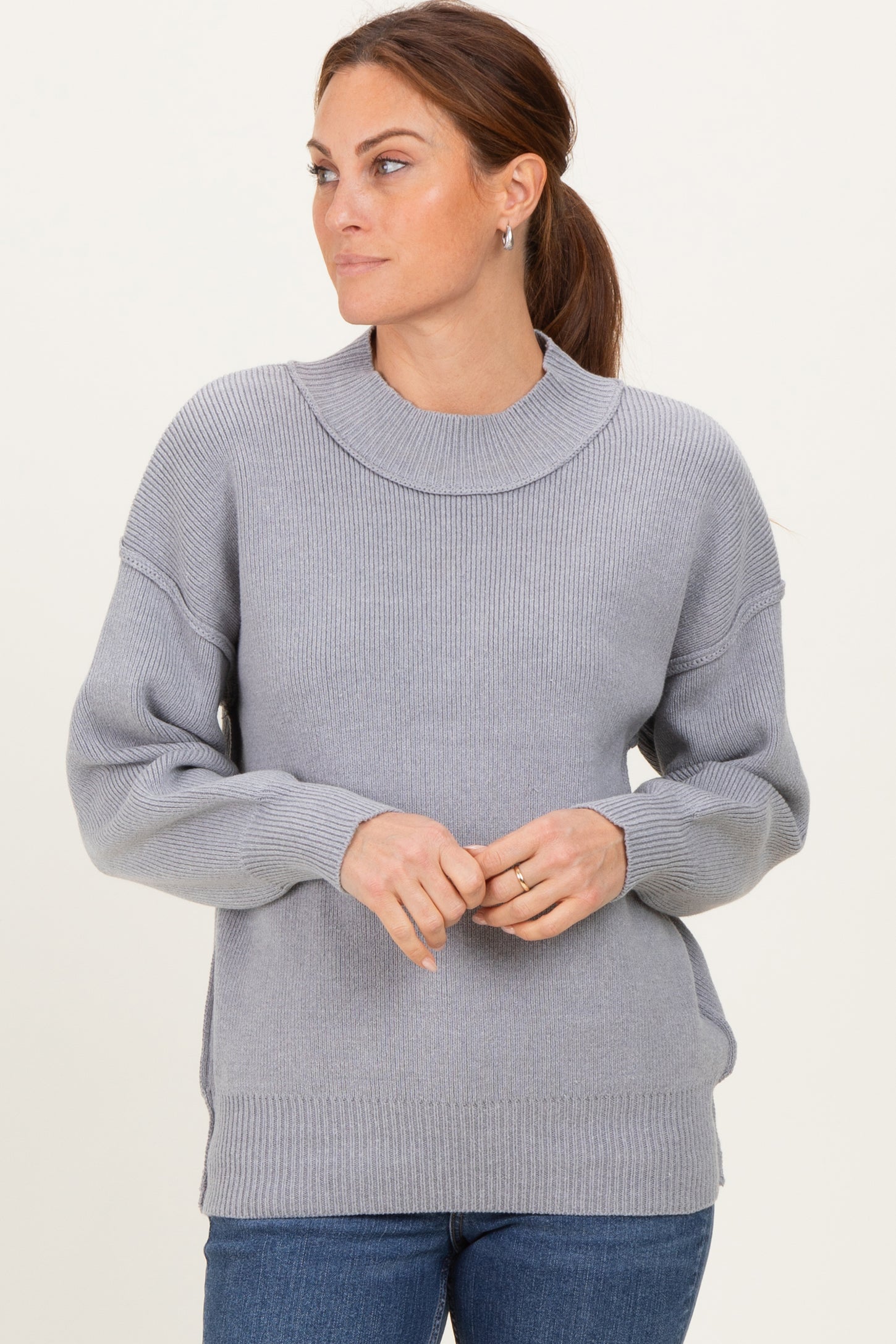 woman wearing a light gray oversized sweater with ribbed texture and a boat neckline, styled with blue jeans
