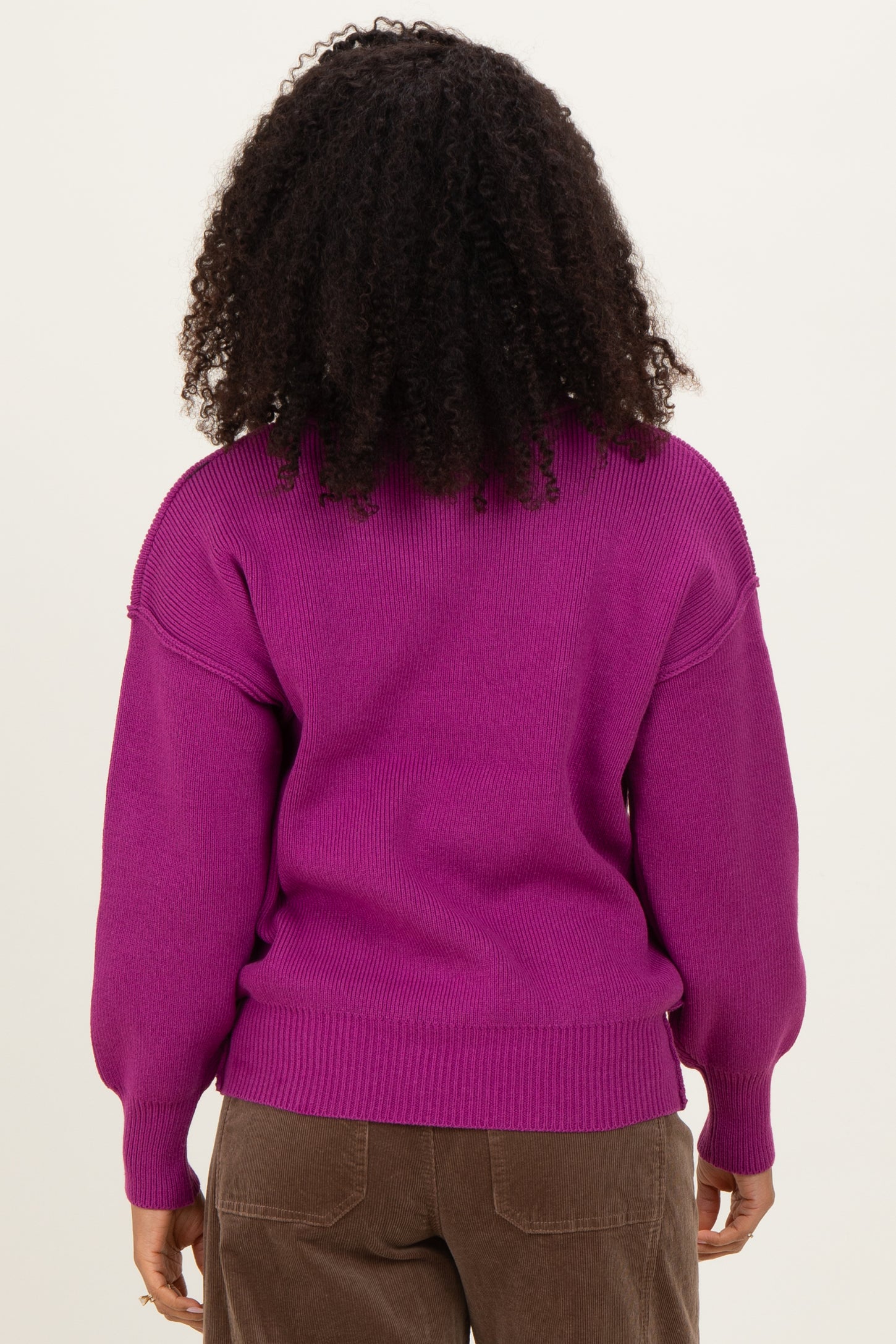 woman wearing a bright purple oversized sweater with puffed sleeves and ribbed hem, showing the back view