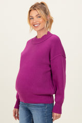 woman wearing a bright pink maternity sweater with a relaxed fit and holding her baby bump