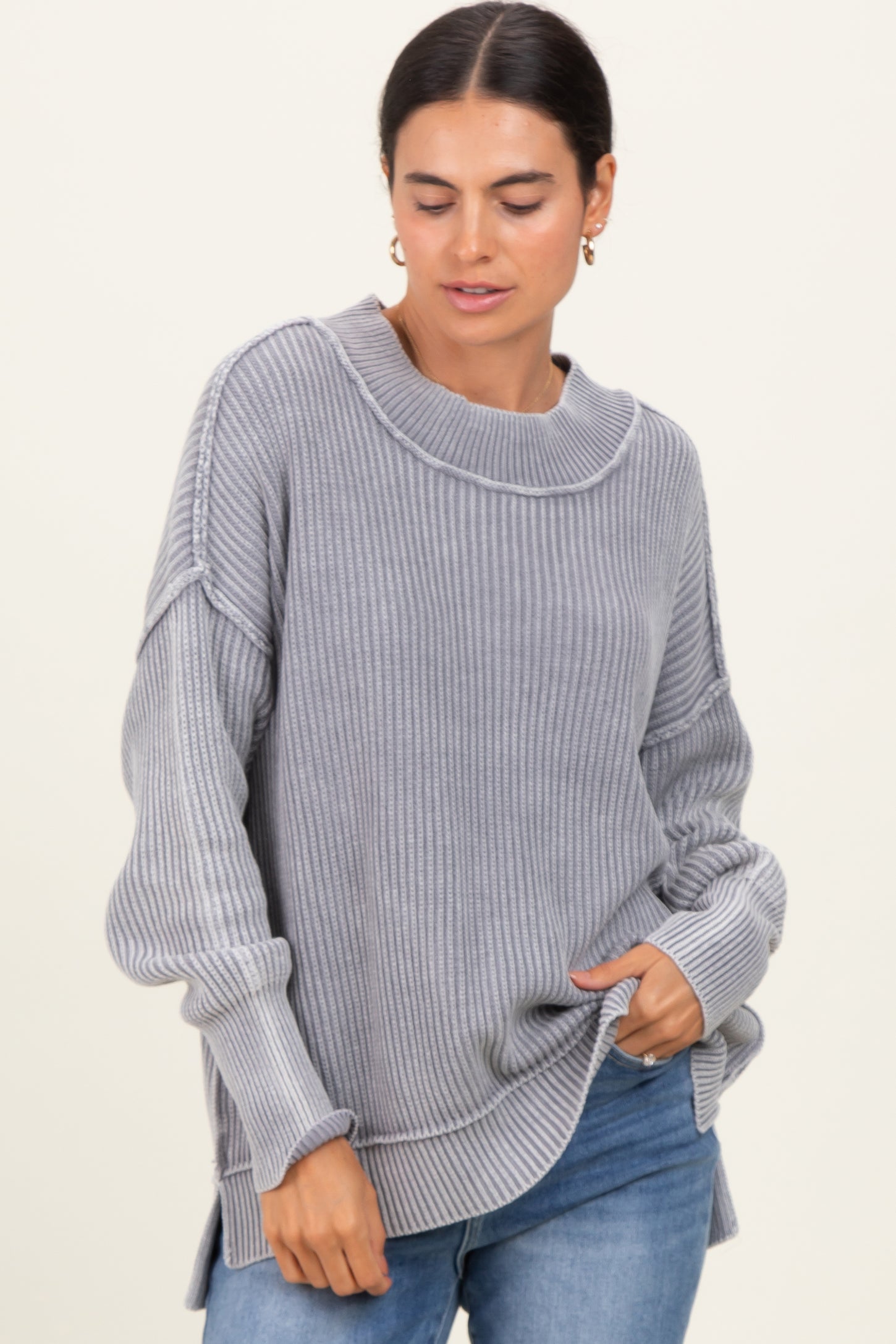 woman wearing a gray ribbed oversized sweater with a boat neckline and side slits, paired with blue jeans