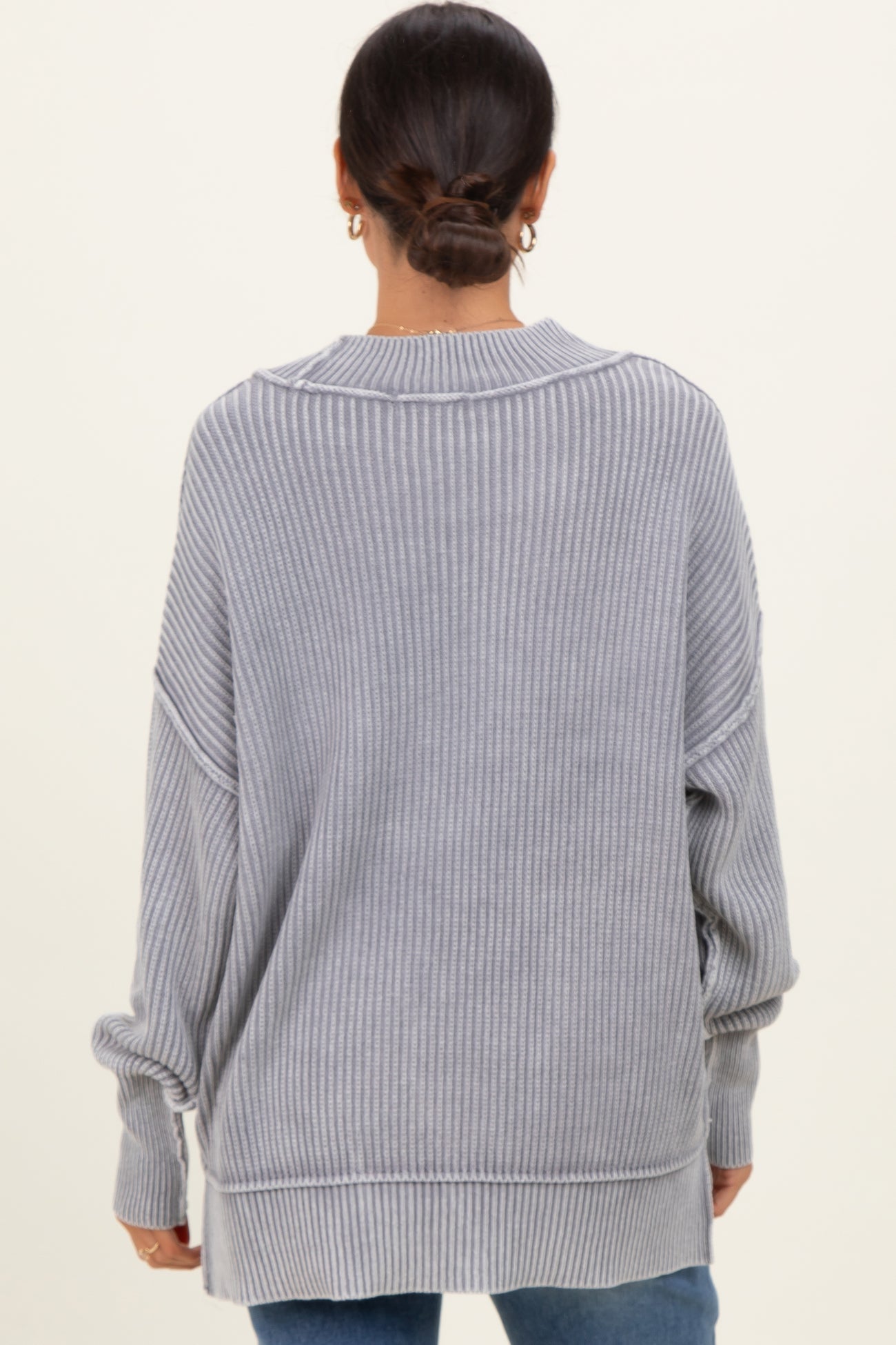 woman wearing a light gray oversized ribbed sweater with dropped shoulders and side slits, viewed from the back