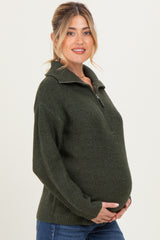 woman wearing a dark green maternity sweater with a half-zip and holding her baby bump