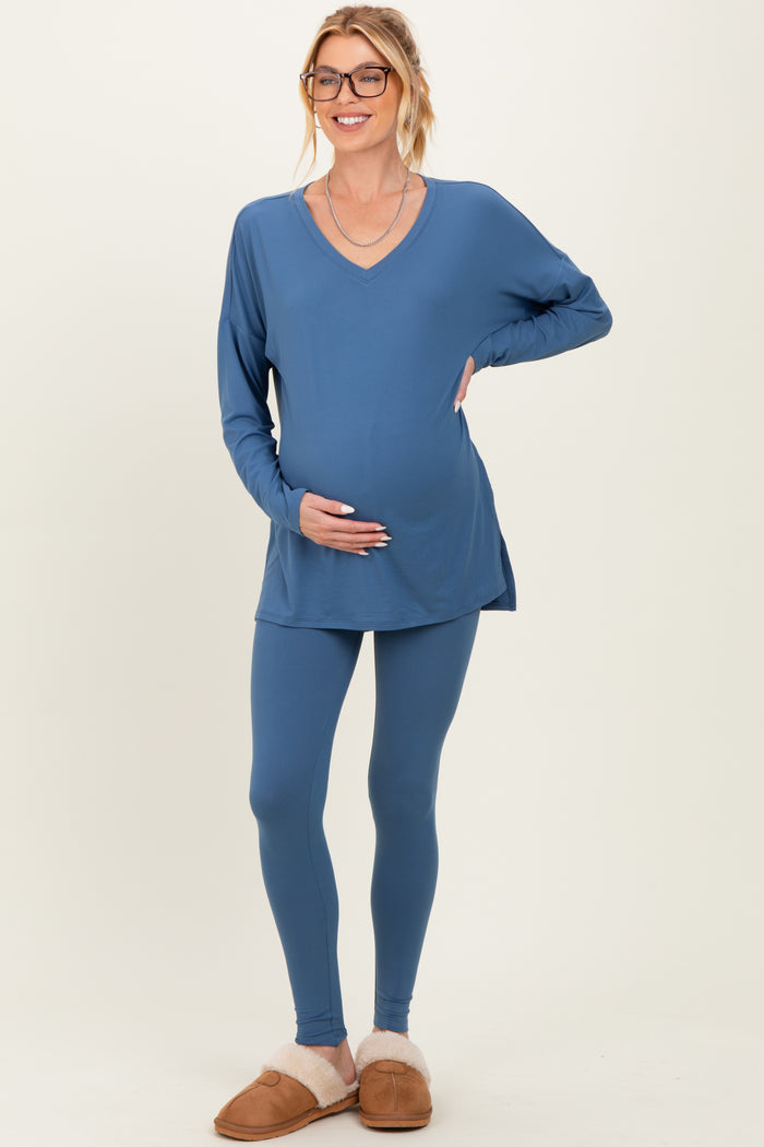 woman wearing a blue long sleeve maternity top and matching leggings, smiling and holding her baby bump