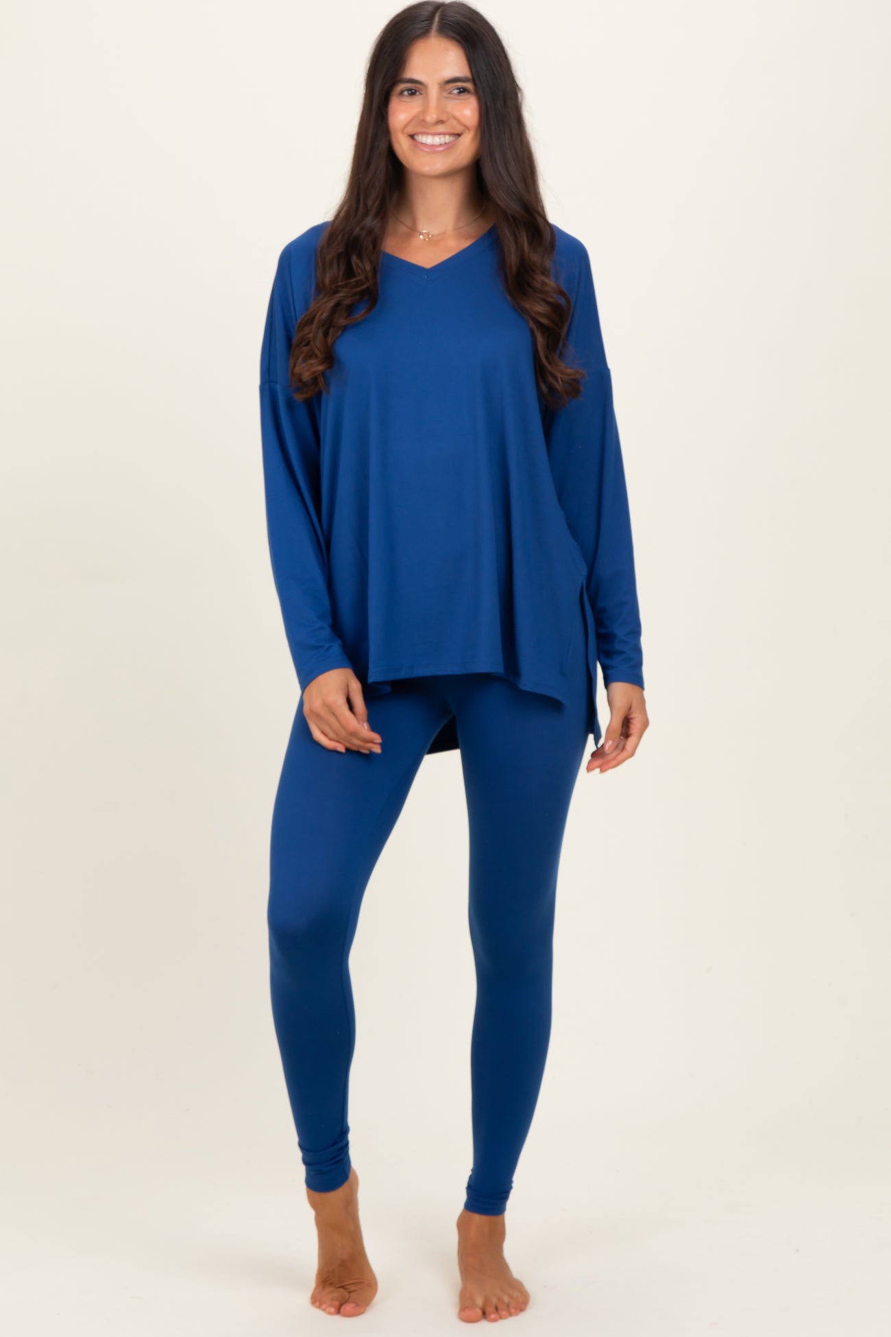 woman wearing a navy blue oversized v-neck top and matching leggings, smiling and standing barefoot