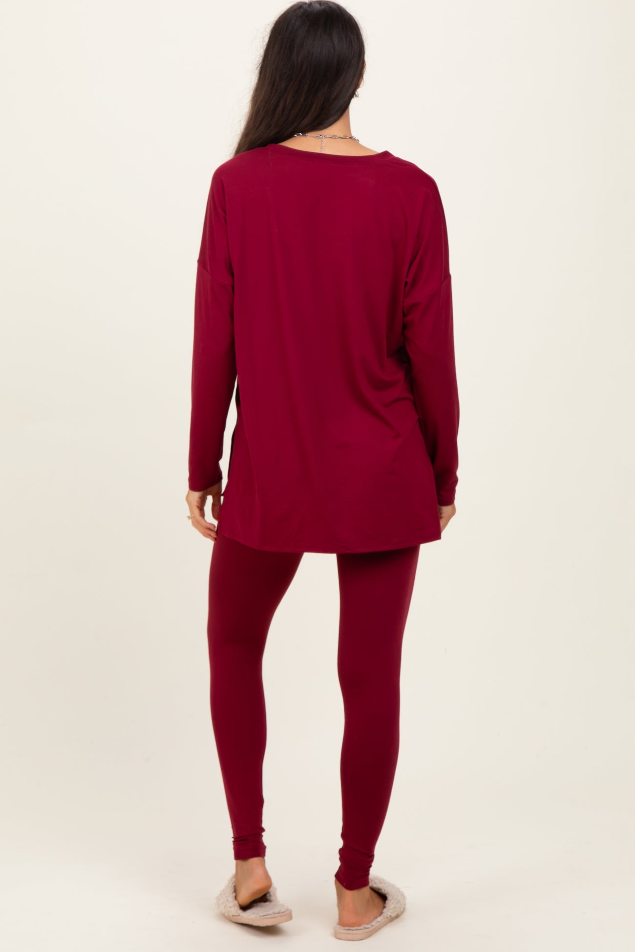 woman wearing a maroon long sleeve top and matching leggings, standing with her back to the camera