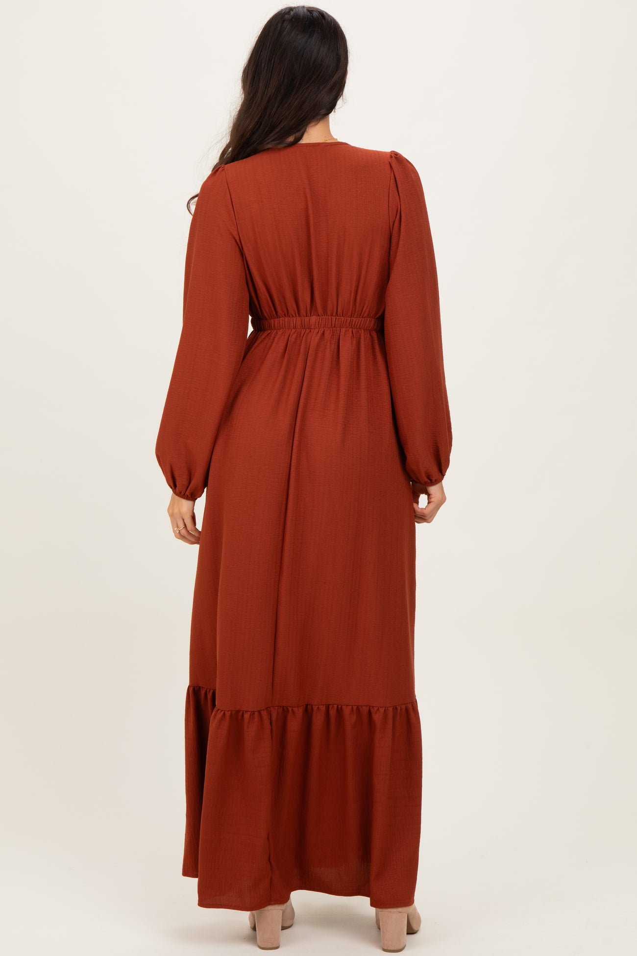 woman wearing a rust long sleeve maxi dress with puff sleeves and a tiered hem, viewed from the back