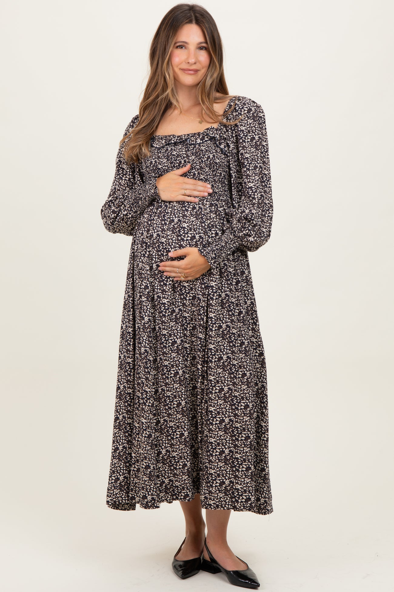woman wearing a black floral maternity maxi dress and holding her baby bump