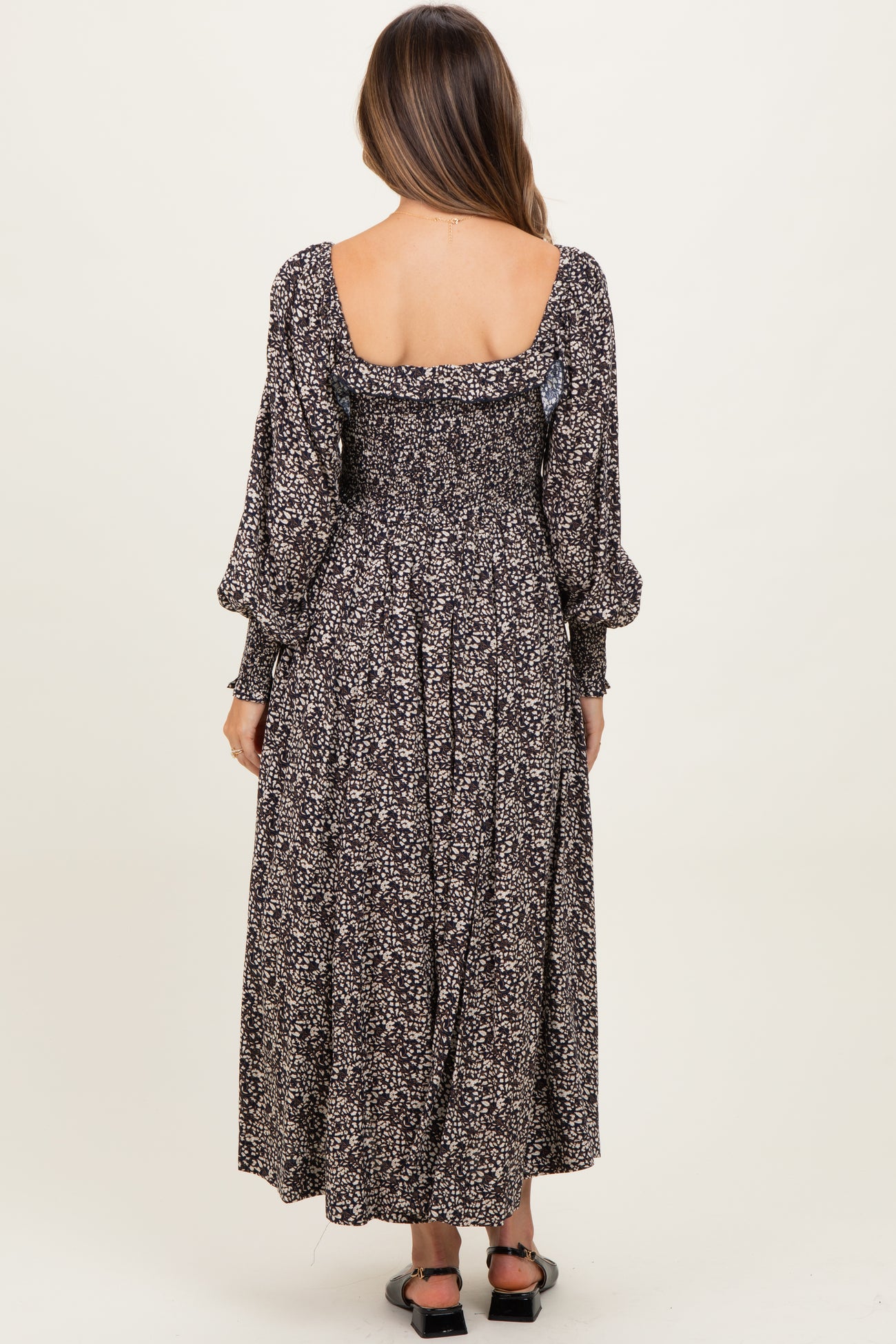 woman wearing a black floral maternity dress with puffed sleeves and a smocked back, showing her baby bump.