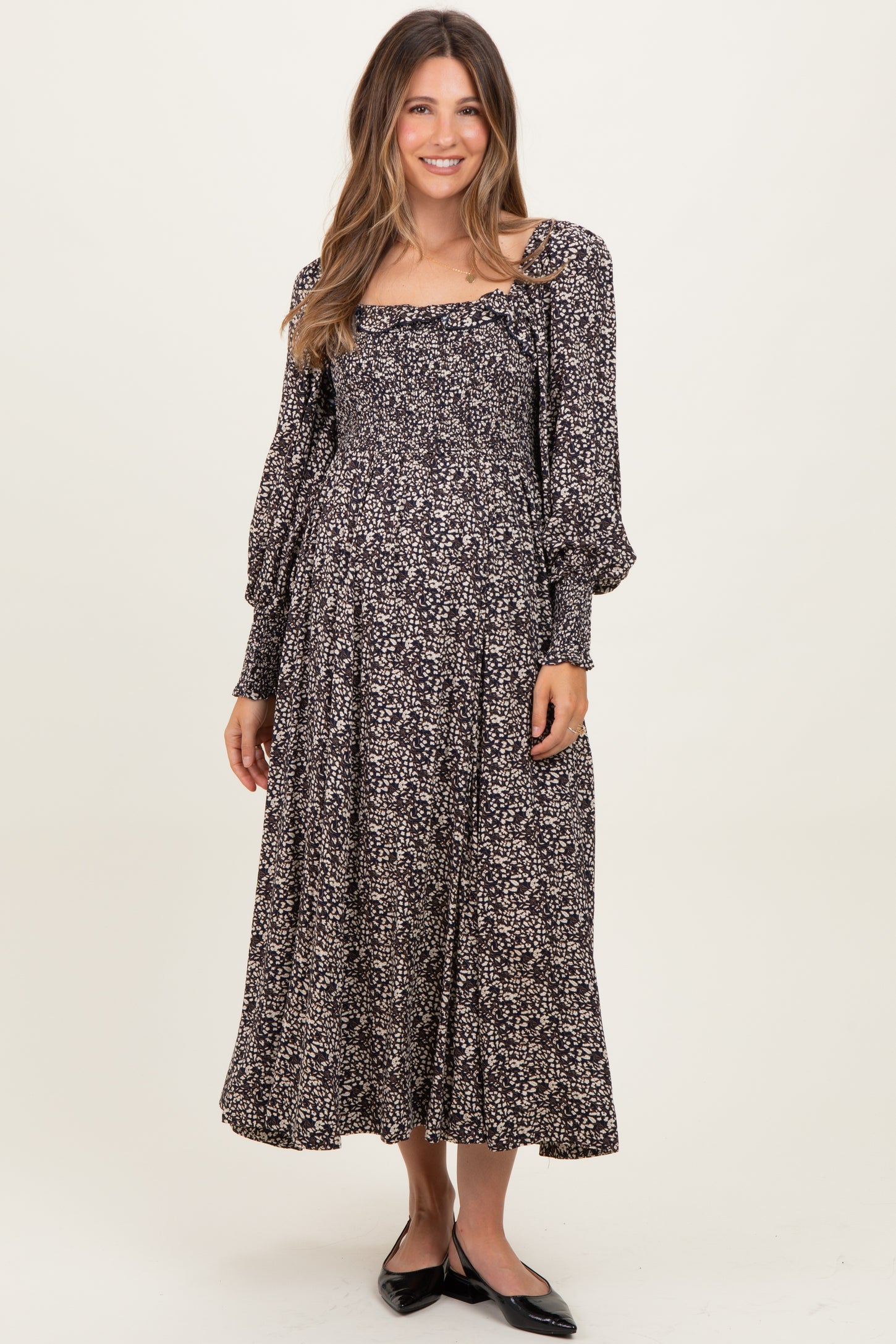 woman wearing a black floral long sleeve maternity dress with a square neckline and flowing skirt, holding her baby bump