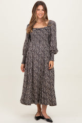 woman wearing a black floral long sleeve maternity dress with a square neckline and flowing skirt, holding her baby bump