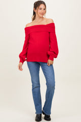 woman wearing a red off-the-shoulder maternity sweater and blue jeans, showing baby bump