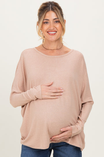 woman wearing a light pink maternity top and holding her baby bump while smiling