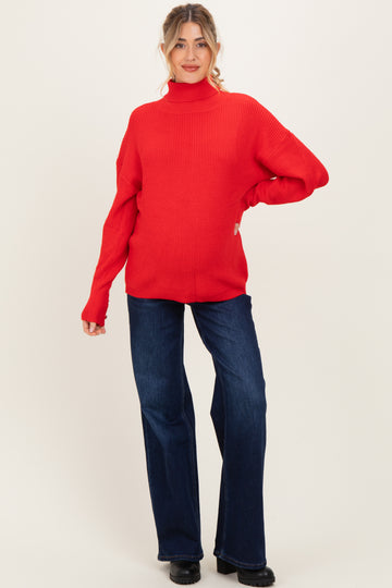 woman wearing a red ribbed turtleneck maternity sweater and flared jeans, showing her baby bump