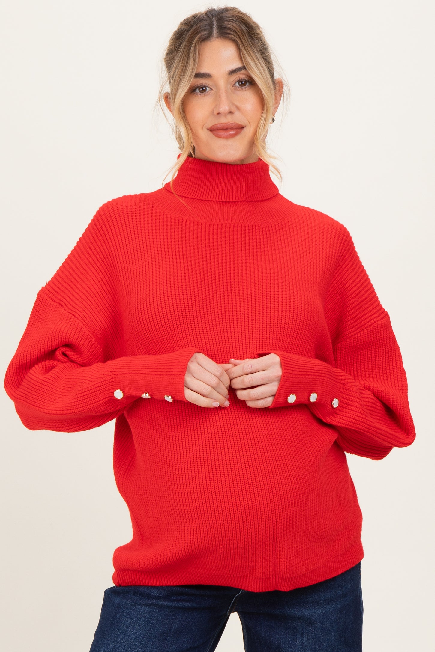 woman wearing a bright red maternity sweater with a high neckline and button details on the sleeves
