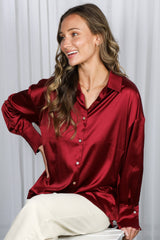 woman wearing a burgundy satin button-up shirt with long sleeves and a relaxed fit, smiling while seated