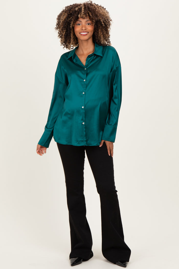 woman wearing a green satin maternity button-up shirt and black flared pants, standing and smiling