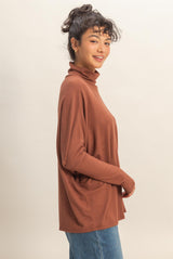 woman wearing a rust turtleneck sweater with relaxed fit and side pockets