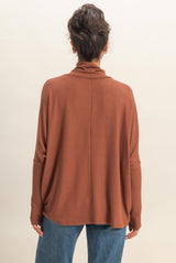woman wearing a rust-colored oversized sweater with a high collar and relaxed fit, seen from the back