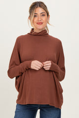woman wearing a rust colored maternity top with a high neckline and relaxed fit, showcasing her baby bump