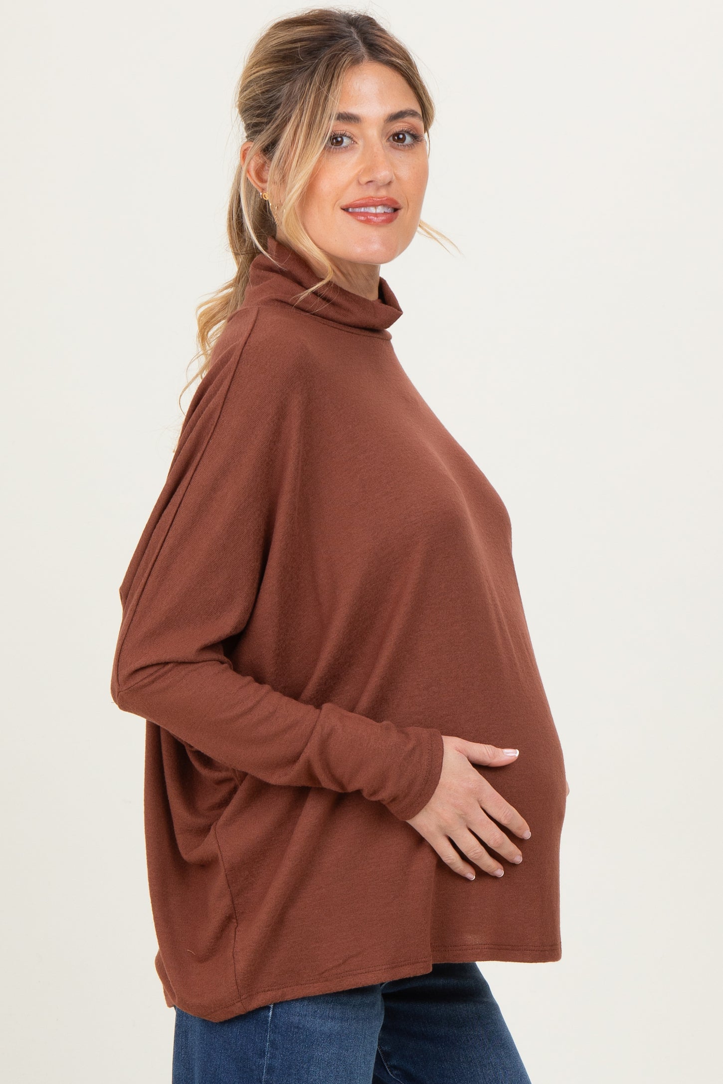 woman wearing a rust-colored maternity top with a turtleneck, gently holding her baby bump