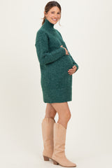 woman wearing a green maternity sweater dress and holding her baby bump, paired with light beige knee-high boots