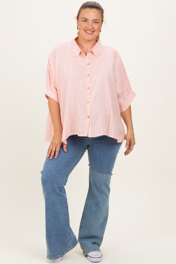 woman wearing a striped pink maternity plus shirt with buttons and rolled sleeves, paired with blue flared jeans