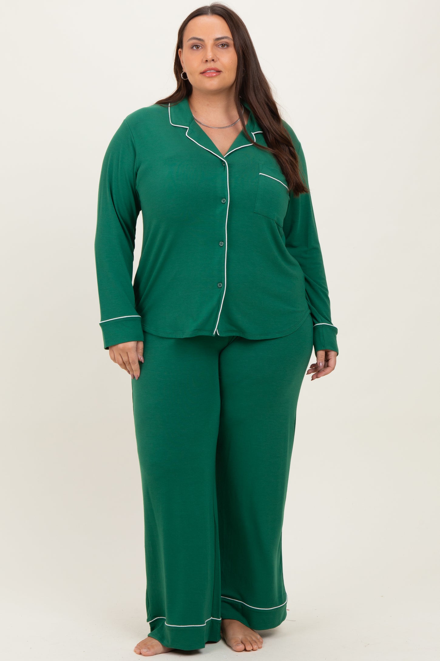 woman wearing a green plus size two-piece pajama set with long sleeves and pants, featuring white piping details