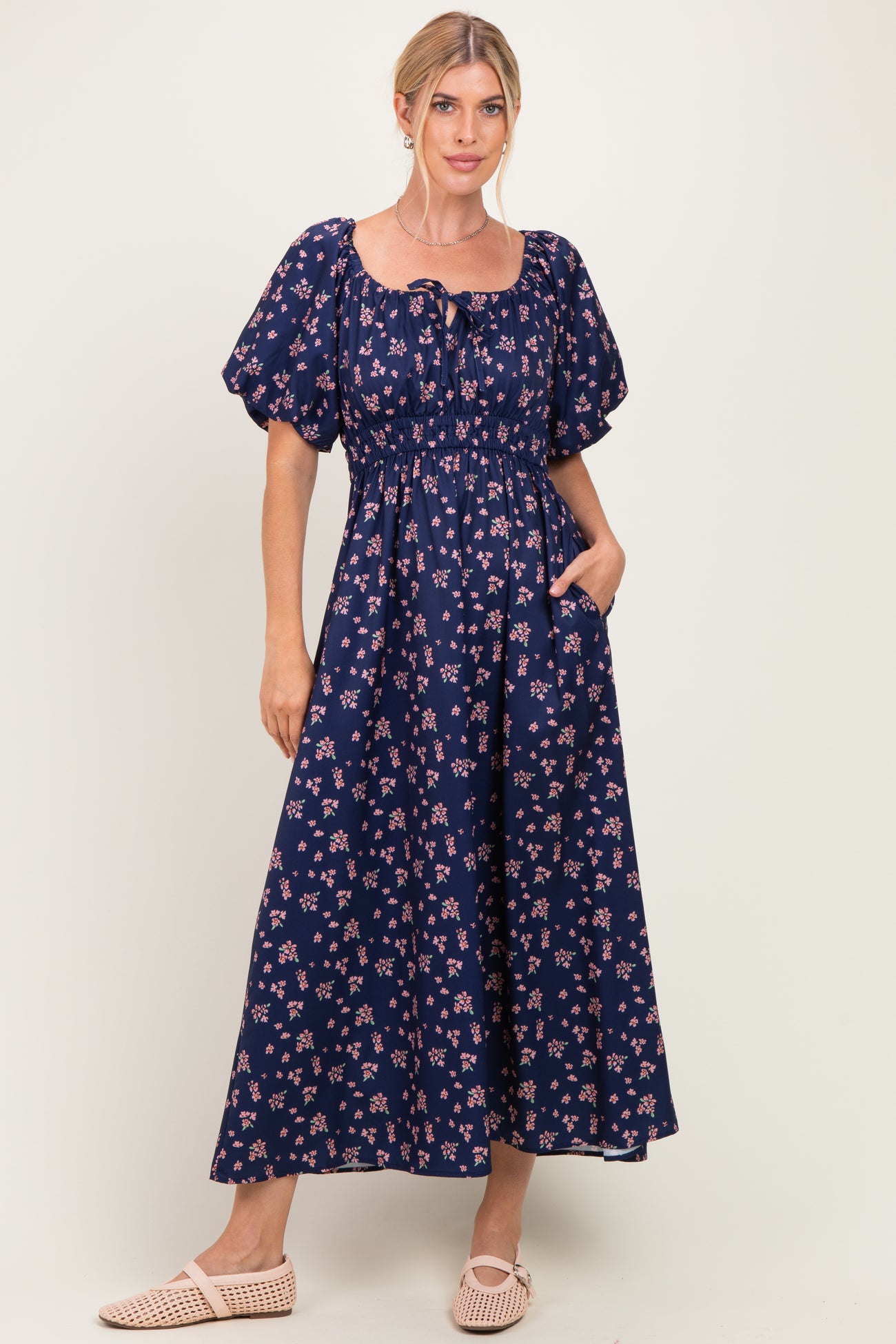 woman wearing a navy blue floral maxi dress with puff sleeves and a cinched waist, posing with hands in pockets