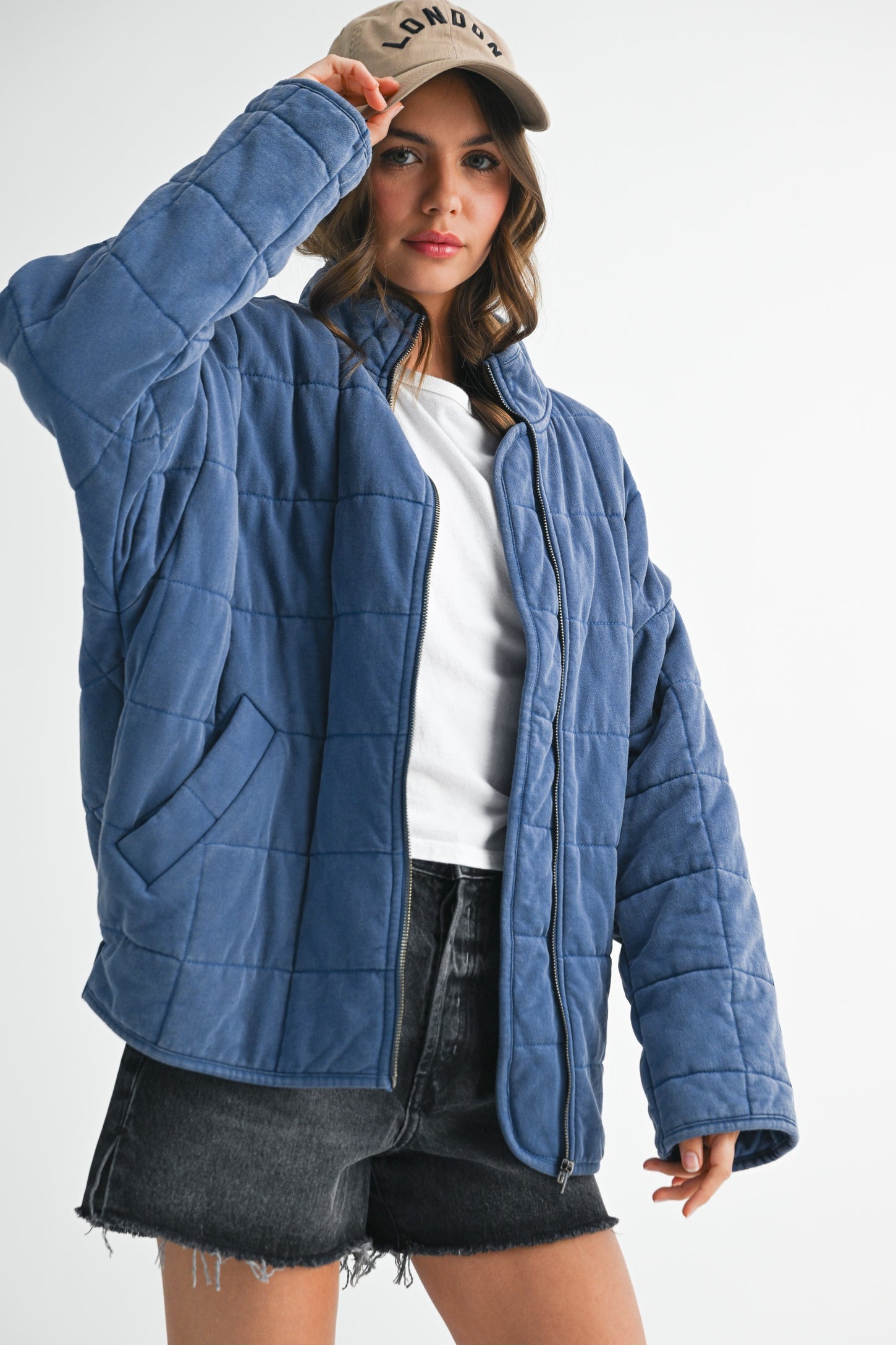 woman wearing a blue quilted jacket with pockets and a baseball cap, styled with a white t-shirt and black shorts
