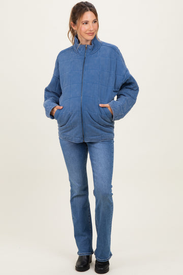 woman wearing a blue quilted maternity jacket with a zip front and pockets, paired with flared jeans and a visible baby bump