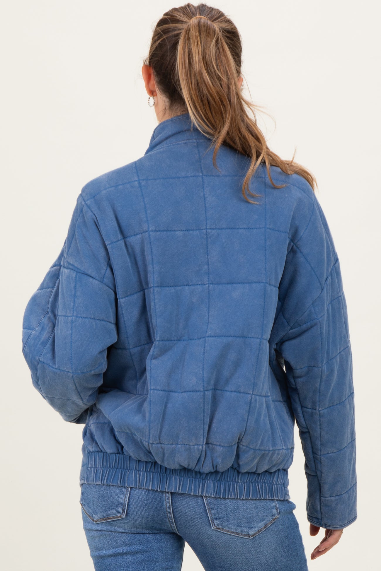 woman wearing a blue quilted maternity jacket with a cinched waist, viewed from the back