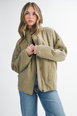 woman wearing an olive green quilted jacket, styled with a high collar, paired with blue jeans