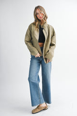 woman wearing an olive green quilted jacket over a black crop top and blue flared jeans