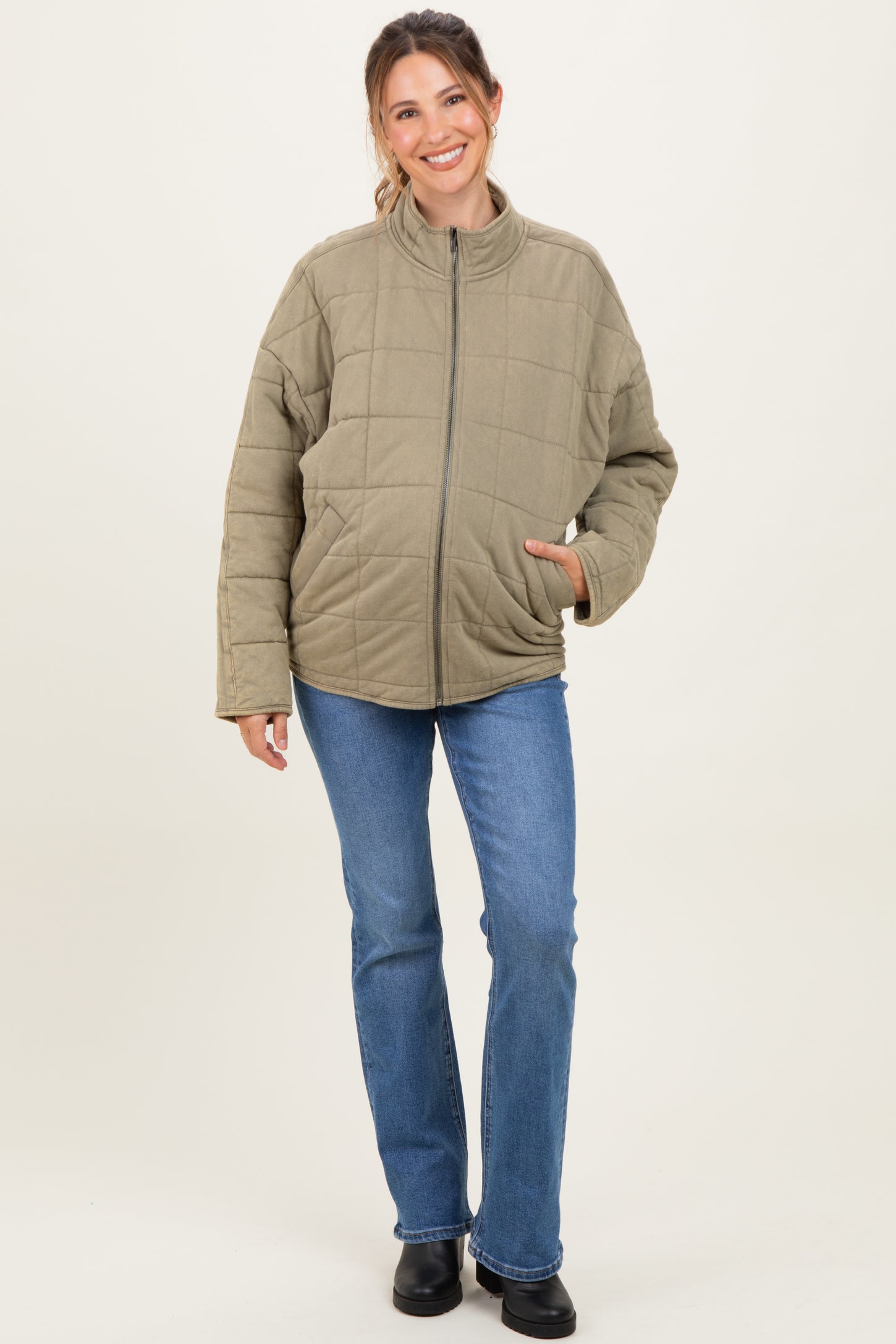 woman wearing a light olive green quilted maternity jacket with a zip-up collar and blue jeans
