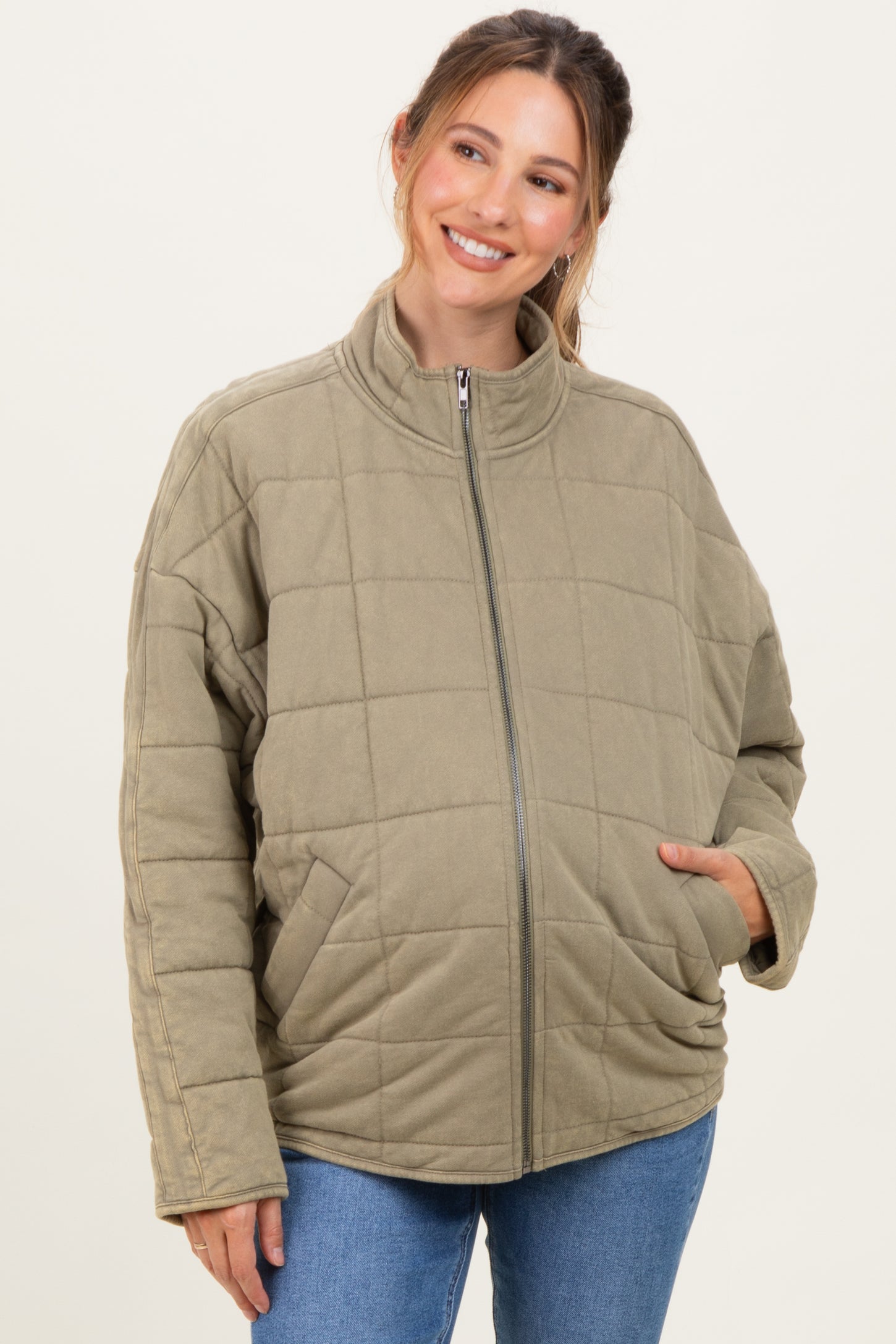 woman wearing a quilted olive green maternity jacket with a front zipper and side pockets, showcasing a baby bump
