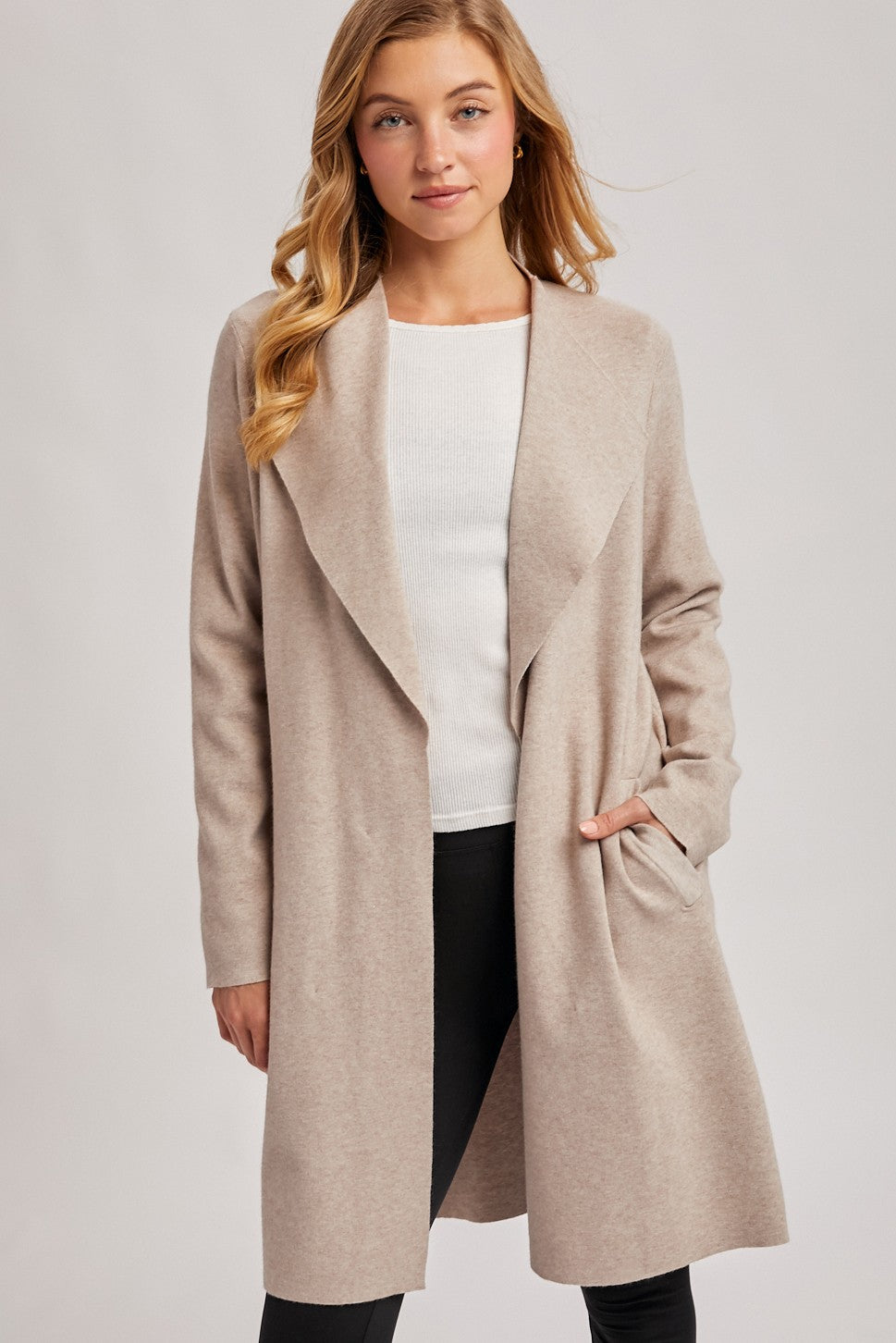 woman wearing a beige long sleeve open front coat over a white sweater and black pants