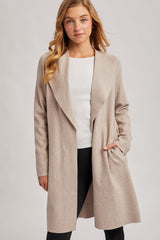 woman wearing a beige long sleeve open front coat over a white sweater and black pants