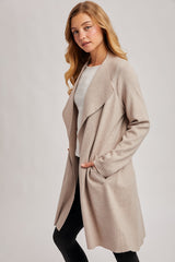 woman wearing a beige open-front cardigan with pockets, styled with a white top and black leggings