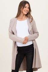 woman wearing a light beige maternity cardigan over a white top and black jeans, smiling with her hands on her waist