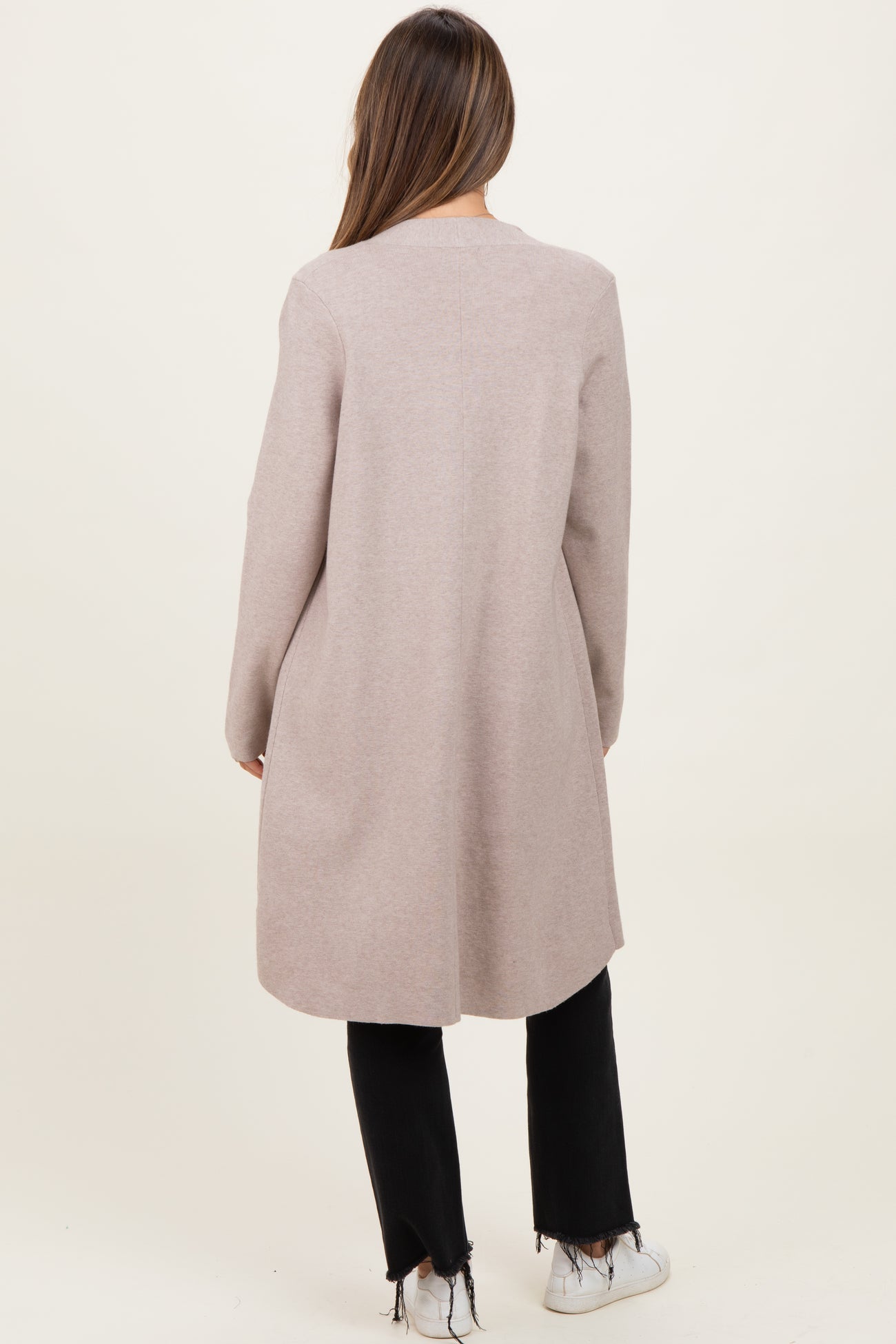 woman wearing a light pink maternity coat, seen from the back, paired with black pants and white sneakers