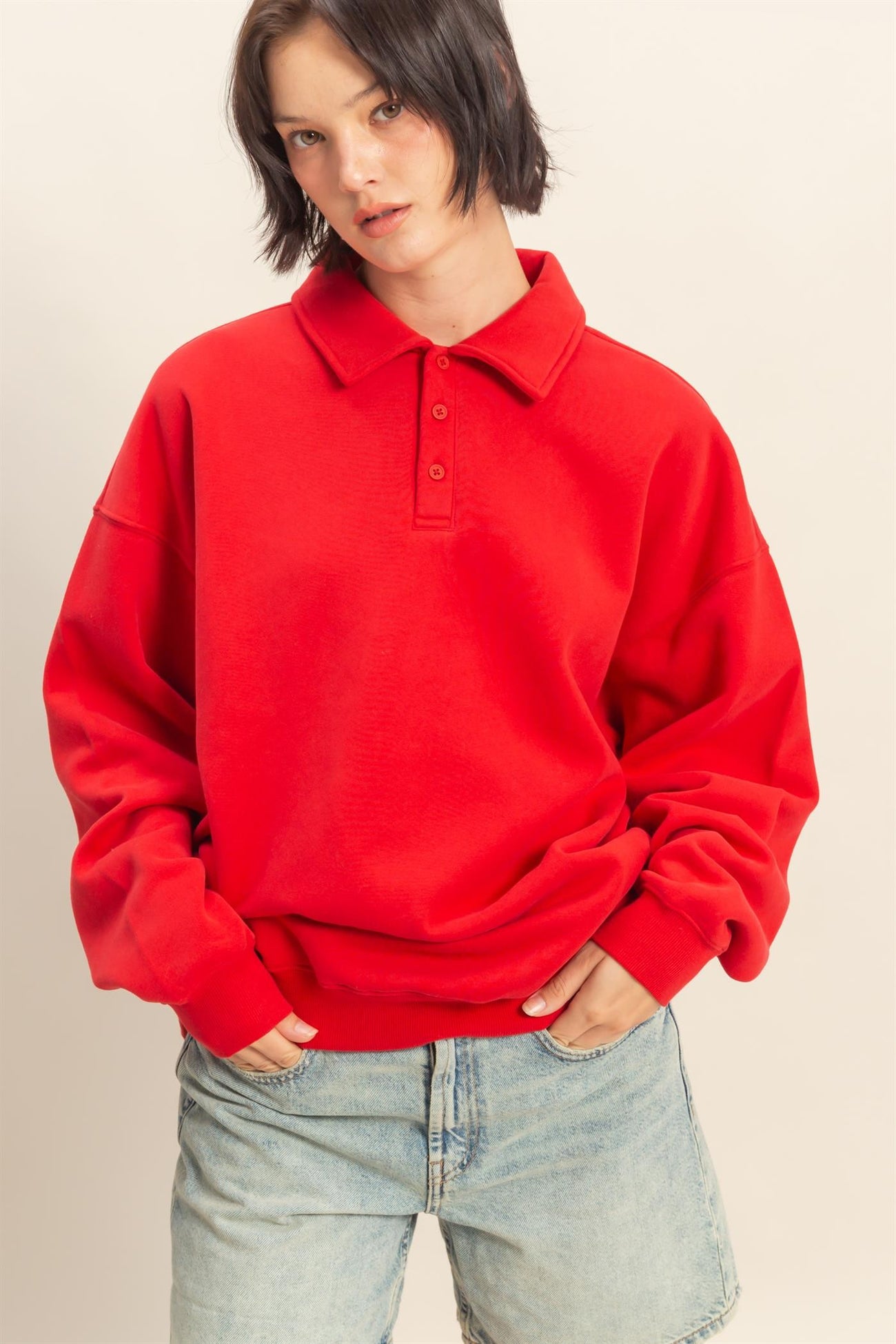 woman wearing a red oversized polo sweatshirt with a collar and three buttons, paired with light blue denim shorts