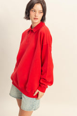 woman wearing a red oversized polo sweatshirt and light wash denim shorts