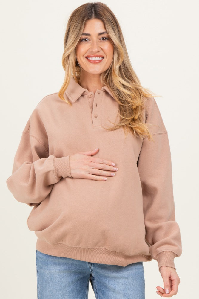 woman wearing a light brown maternity polo sweatshirt and holding her baby bump